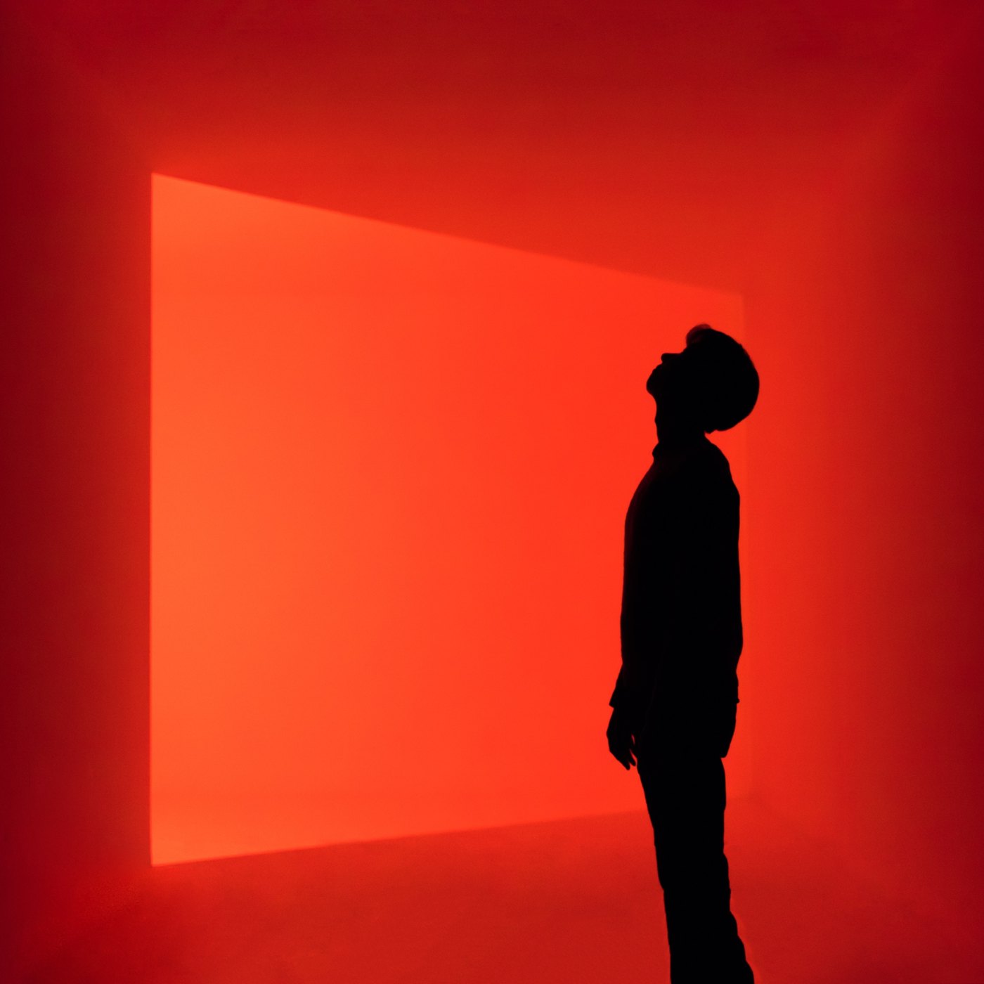 A figure in silhouette looks up at a rectangle of red light